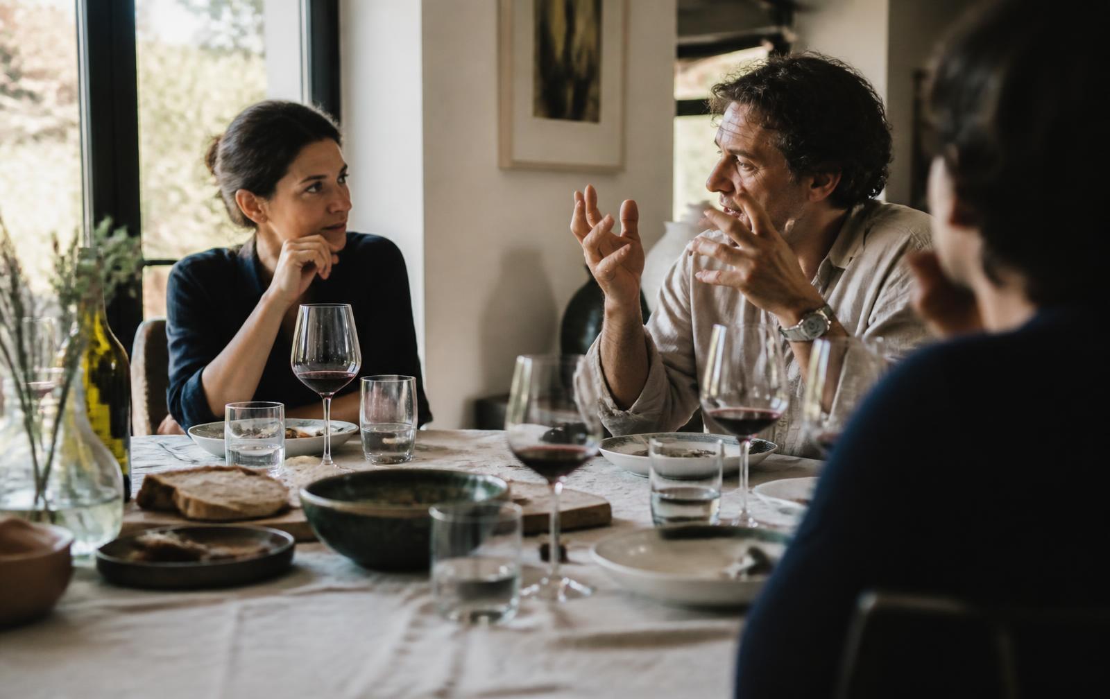 Sobremesa en casa con luz natural, pan, vino y conversación entre varias personas