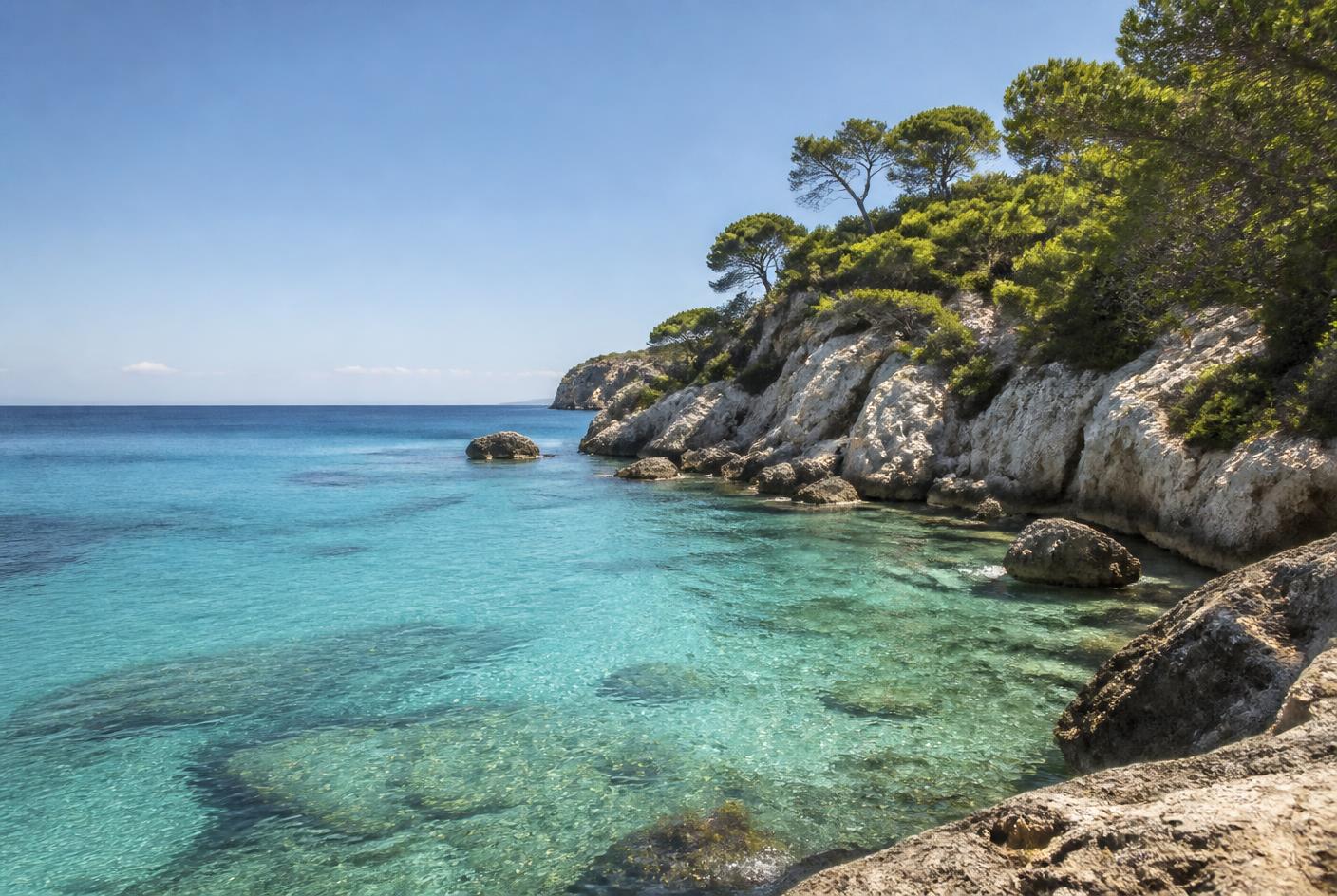 Cala menorquina de agua turquesa entre rocas calizas y pinos