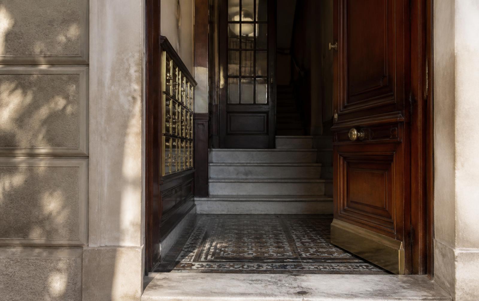 Portal de un edificio residencial madrileño con suelo hidráulico, buzones de latón y escalera de mármol