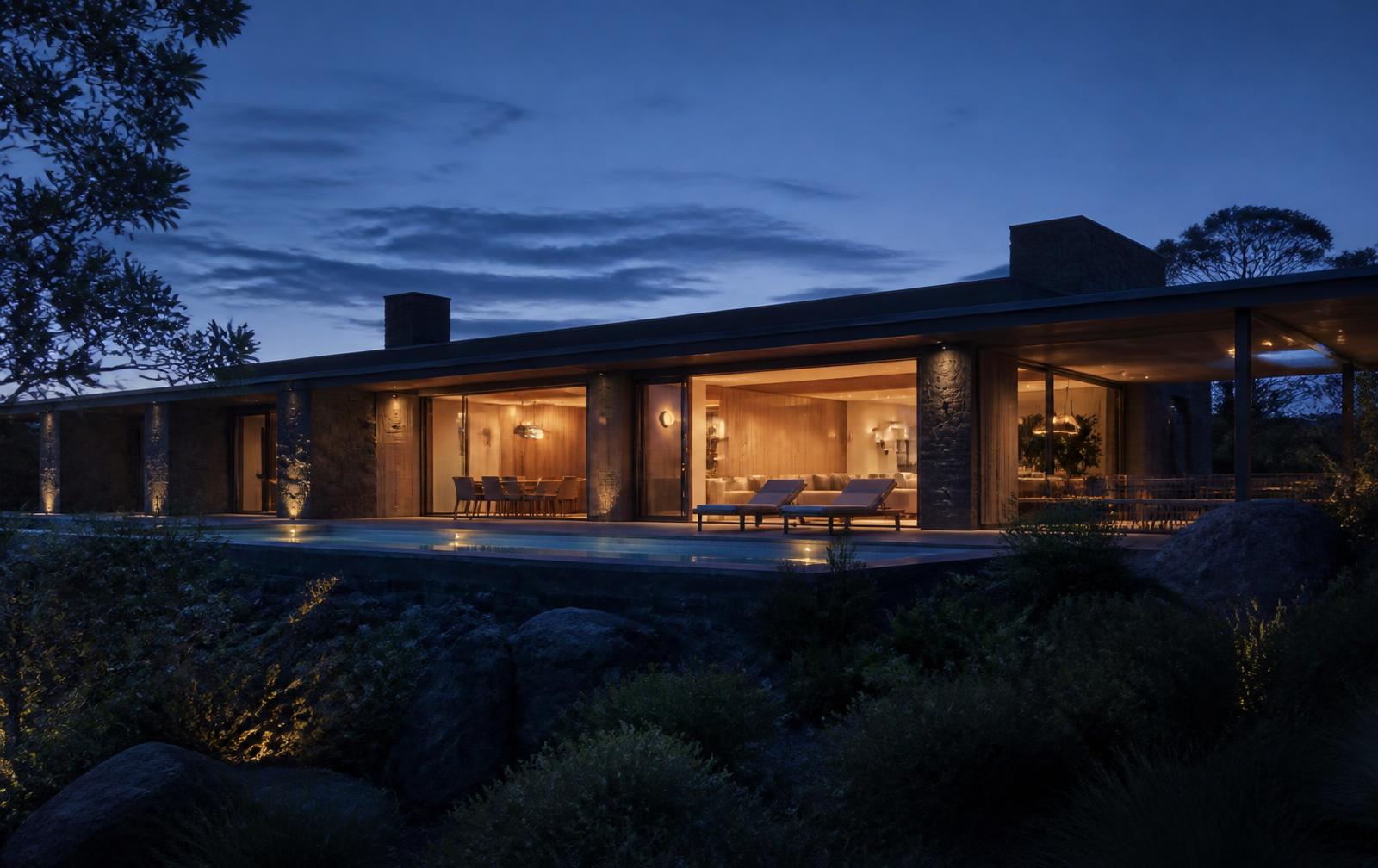 Vivienda contemporánea al anochecer con la luz interior cálida saliendo por los grandes huecos hacia el paisaje