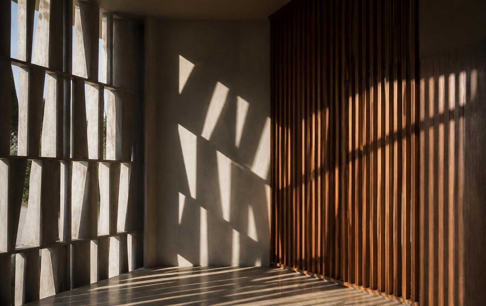 Celosía de hormigón y lamas de madera proyectando sombras gráficas sobre una pared y el pavimento