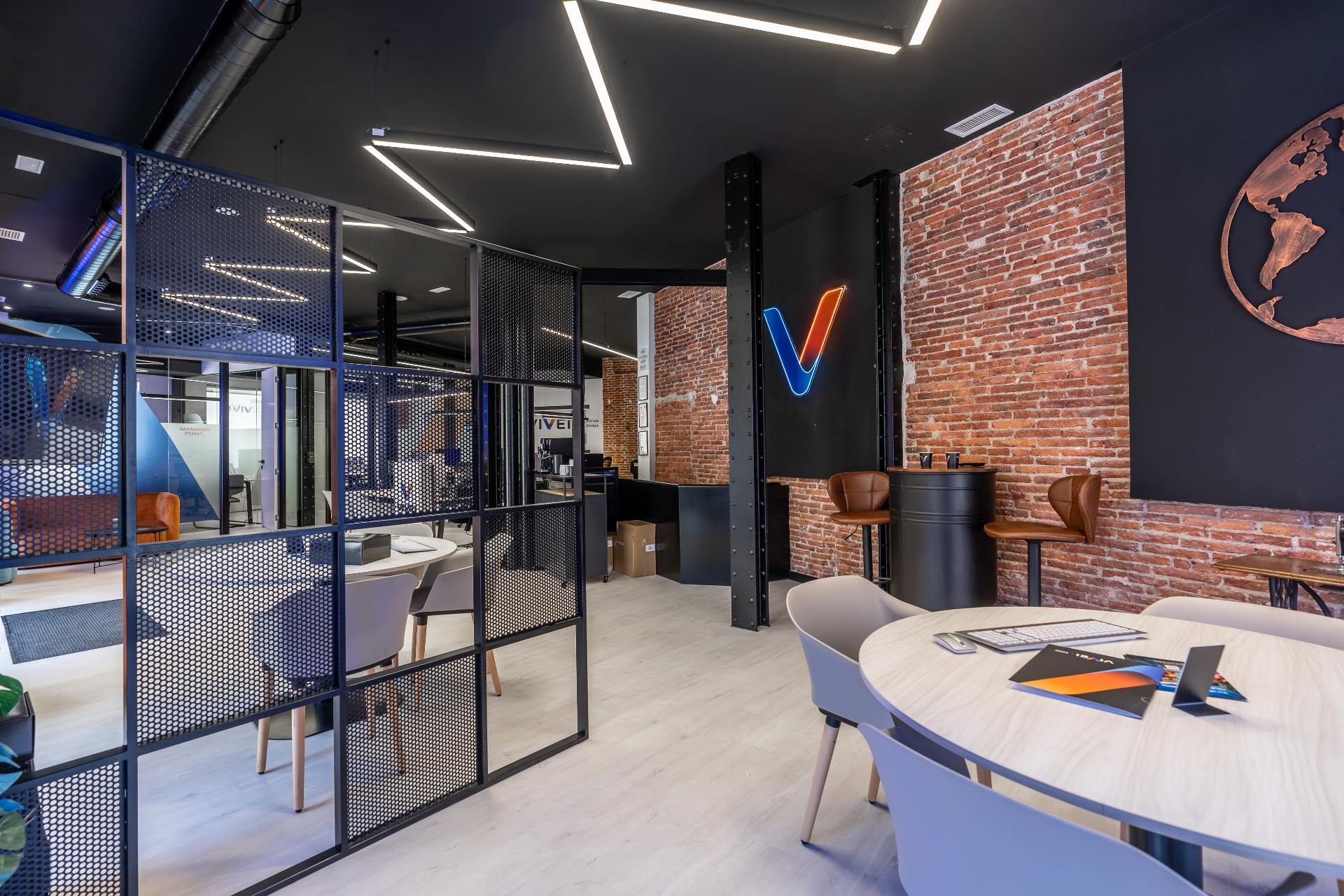 Interior de la oficina Vivei Latina con muro de ladrillo, logo V iluminado y zona de trabajo